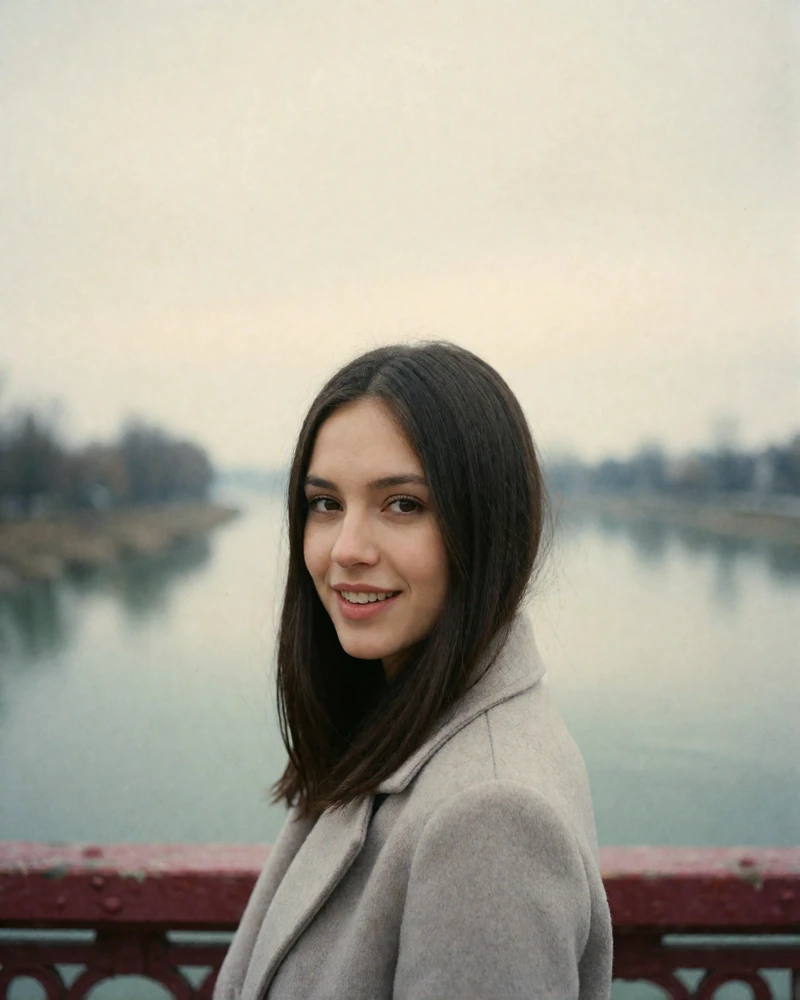 Romanian woman with straight dark hair in a grey coat standing on a river bridge, verified member portrait